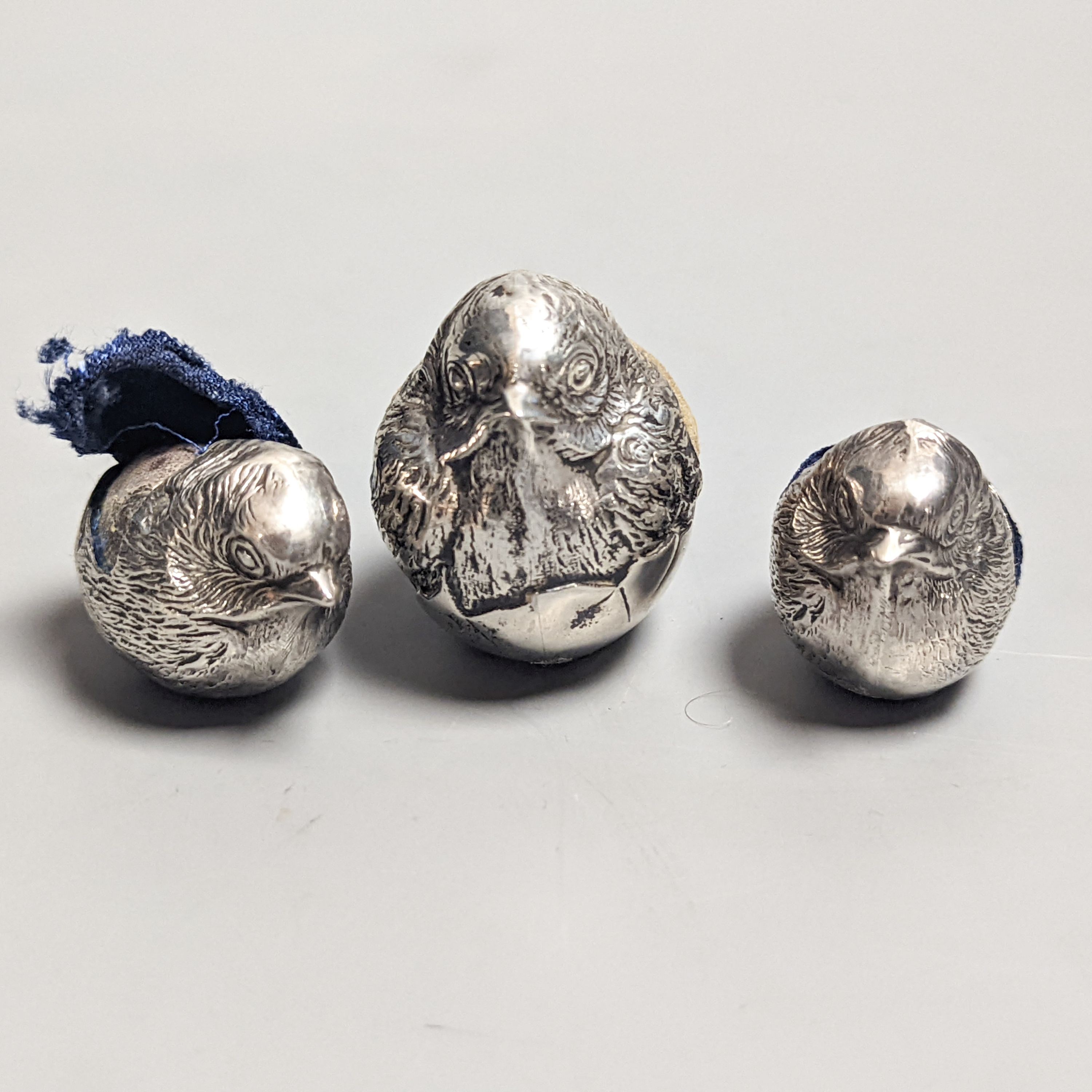 A suite of three Edwardian novelty silver mounted chick pin cushions, by Sampson Mordan & Co, Chester, 1907, height 43mm(1) & 33mm(2).